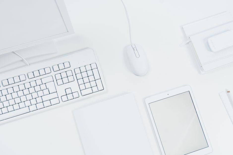 A clean, minimalist workspace featuring a keyboard, mouse, and tablet on a white desk.